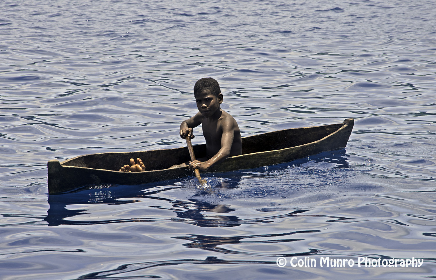 A local boy in a dugout canoe paddles by us. Garove Island, Vitu Islands, Bismark Sea, Papua New Guinea. Copyright Colin Munro